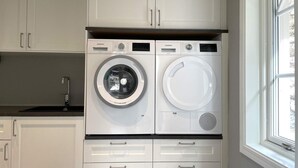 A compact laundry room with two front-loading washing machines, a sink, and a window. - 5 Star Holiday Home in Uddevalla (Uddevalla)