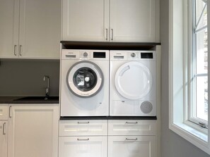 A compact laundry room with two front-loading washing machines, a sink, and a window.