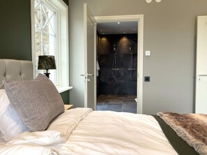 A bedroom with a bed, a nightstand, a lamp, and a view into a bathroom with a shower.