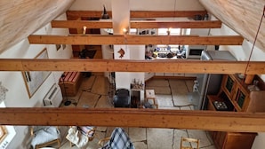 Een meerlaags houten interieur met een keuken op de begane grond, een eetgedeelte op de bovenverdieping en een zolderruimte met een raam.