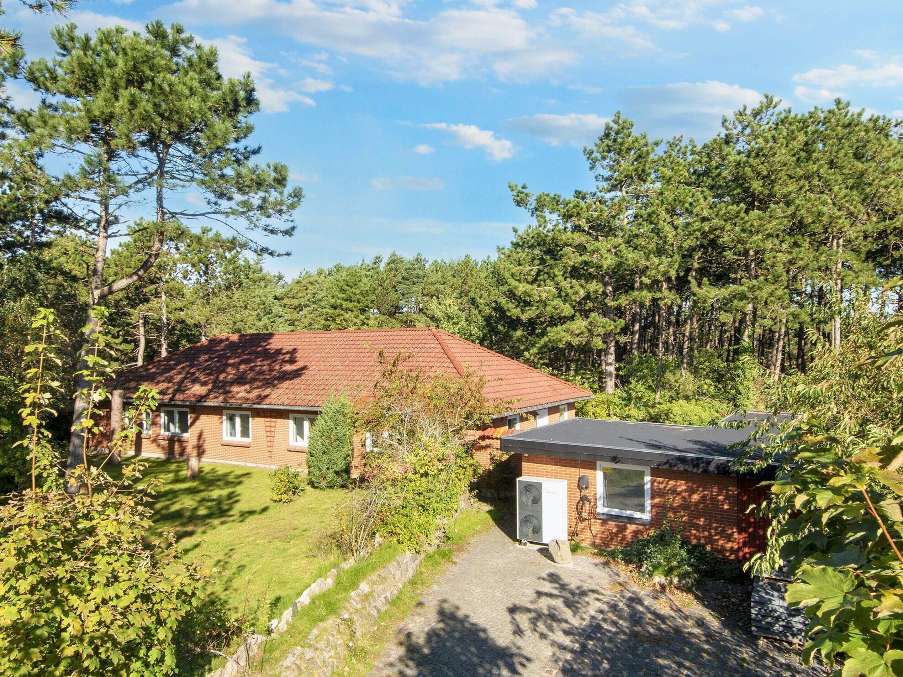 Ett hus med en fasad av tegel, ett rött tak och ett litet garage som är byggt ihop med huset.