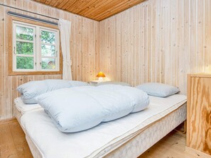 Ein Einzelbett mit weißer Bettwäsche und Kissen, eine Nachttischlampe und ein Fenster mit Vorhängen.