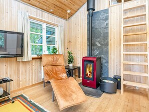 Ett mysigt rum med en läderfåtölj, en tv, en öppen spis och ett fönster med gardiner.
