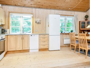 Eine Küche mit Holzschränken, einem Bosch-Kühlschrank, einem Geschirrspüler sowie einem Essbereich mit Holztischen und einem Tisch.