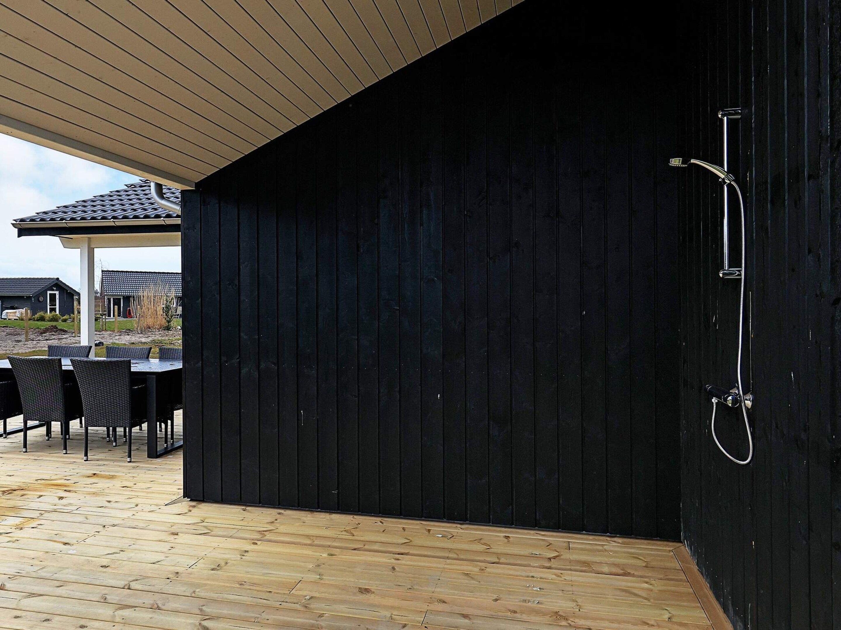 Un espace extérieur abrité, doté d’une terrasse en bois, d’un mur noir et d’une douche.