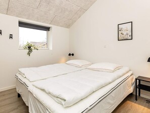 A bedroom with a bed, a window with a view, a wall-mounted lamp, and a framed picture.