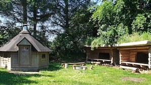 A rustic cabin with a small porch and a chimney, surrounded by a grassy area with trees. - 8 Person Holiday Home in Henne (Henne)