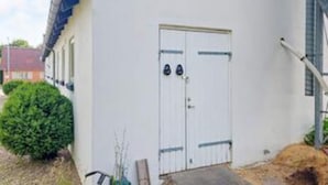 A white building with a double door, a small step leading up to the entrance, and a bush in the foreground. - 8 Person Holiday Home in Henne (Henne)