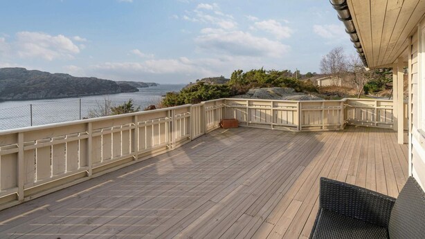 Eine Holterrasse mit Geländer, die auf ein Gewässer und Hügel blickt.