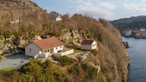 Ein Küstengebiet mit einem Haus, das ein rotes Dach, eine Veranda und eine kleine Terrasse hat.