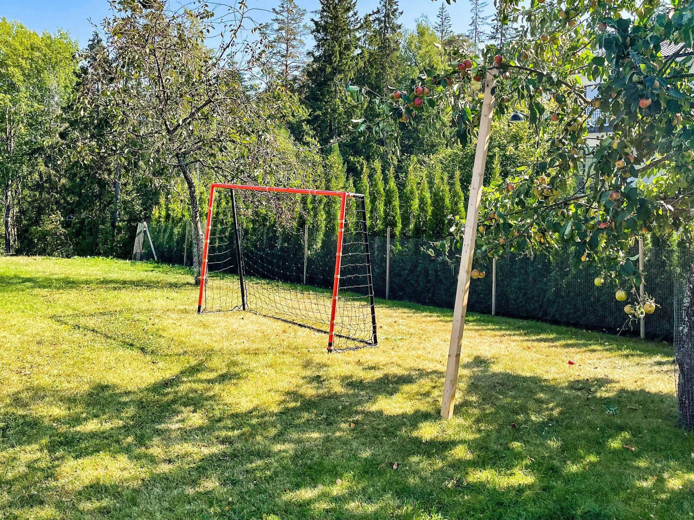 A grassy area with a red goalpost and a tree bearing fruit.