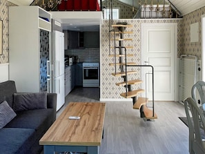 A compact living space with a kitchenette, a sofa, a coffee table, and a spiral staircase.