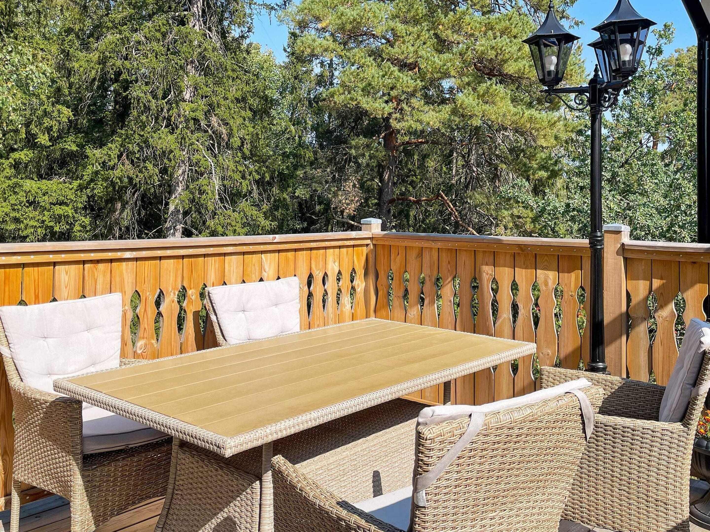 Een terras buiten met een houten terras, rieten meubels en een tafel.