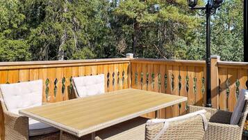 Een terras buiten met een houten terras, rieten meubels en een tafel.