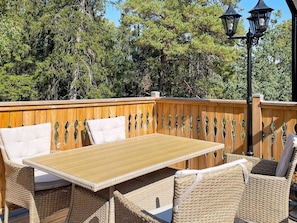 An outdoor patio with a wooden deck, wicker furniture, and a table.