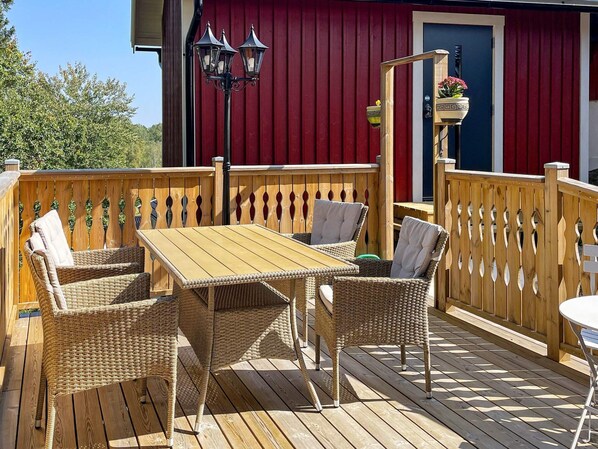 Une terrasse en bois avec des meubles en osier et une table, un bâtiment rouge en arrière-plan et un lampadaire noir.