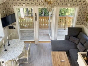 A room with a sofa, a table, a TV, and a balcony with a wooden railing. - 4 Person Holiday Home in Huddinge (Huddinge)