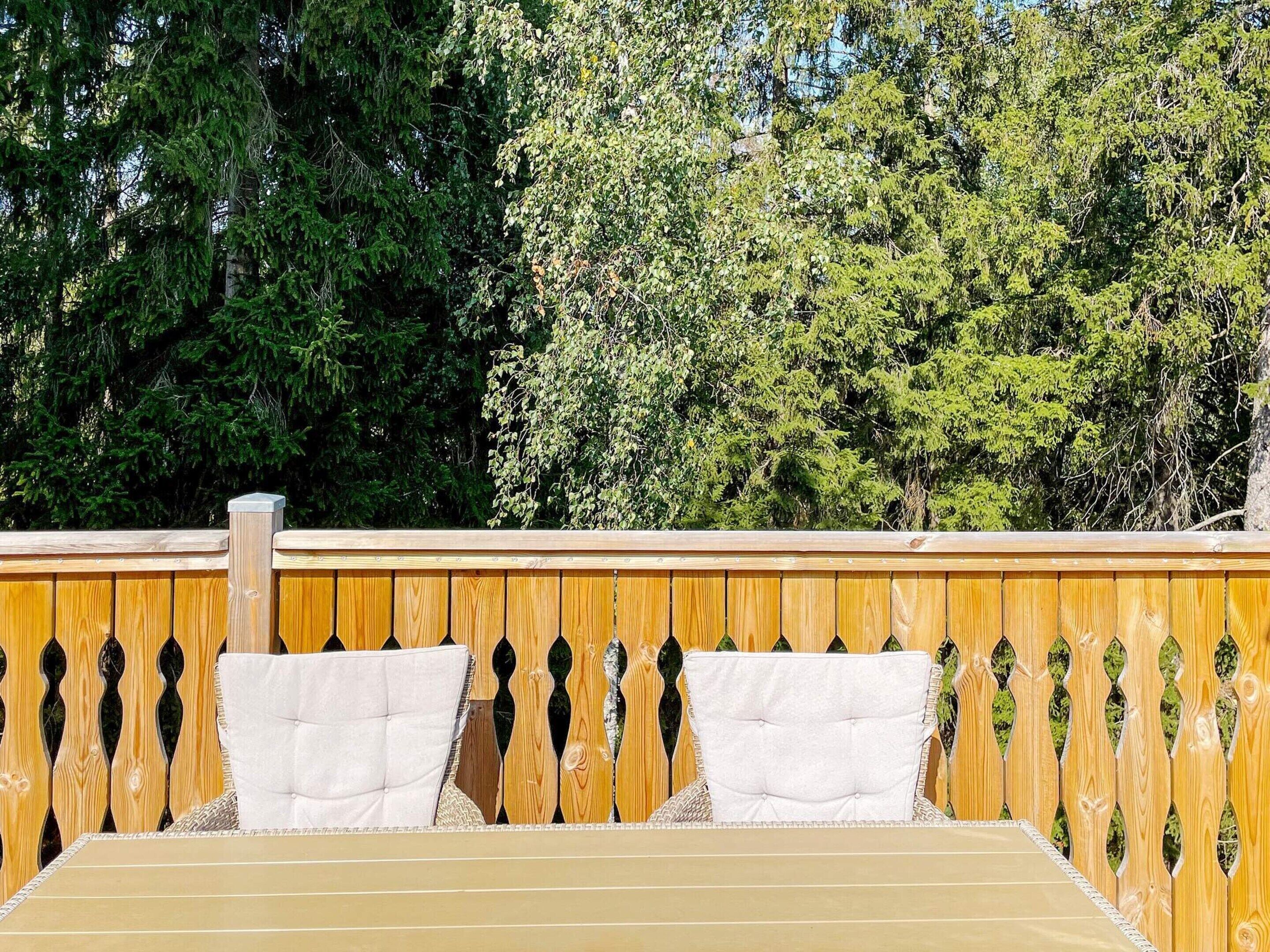 A wooden deck with a bench and cushions, surrounded by trees.
