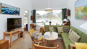 A living room with a television, sofa, chairs, a table, and artwork on the walls. - 5 Star Holiday Home in Gilleleje (Gilleleje)