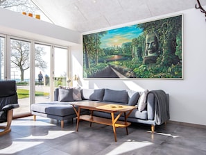 A modern living room with a large painting, a sofa, a coffee table, and a view through the glass door. - 8 Person Holiday Home in Odder (Odder)