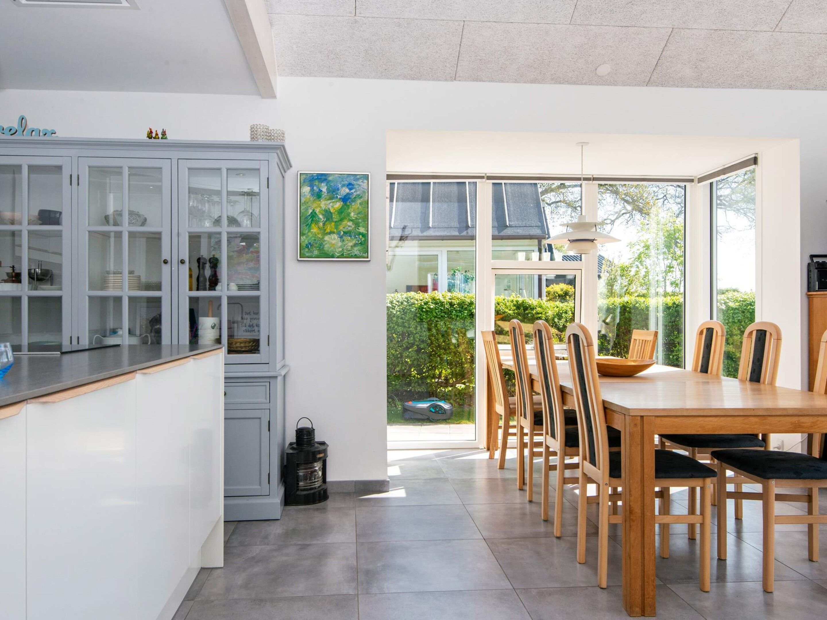 A modern kitchen with a dining area, featuring a large window, a cabinet with glass doors, and a table with chairs.