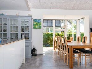 A modern kitchen with a dining area, featuring a large window, a cabinet with glass doors, and a table with chairs. - 8 Person Holiday Home in Odder (Odder)