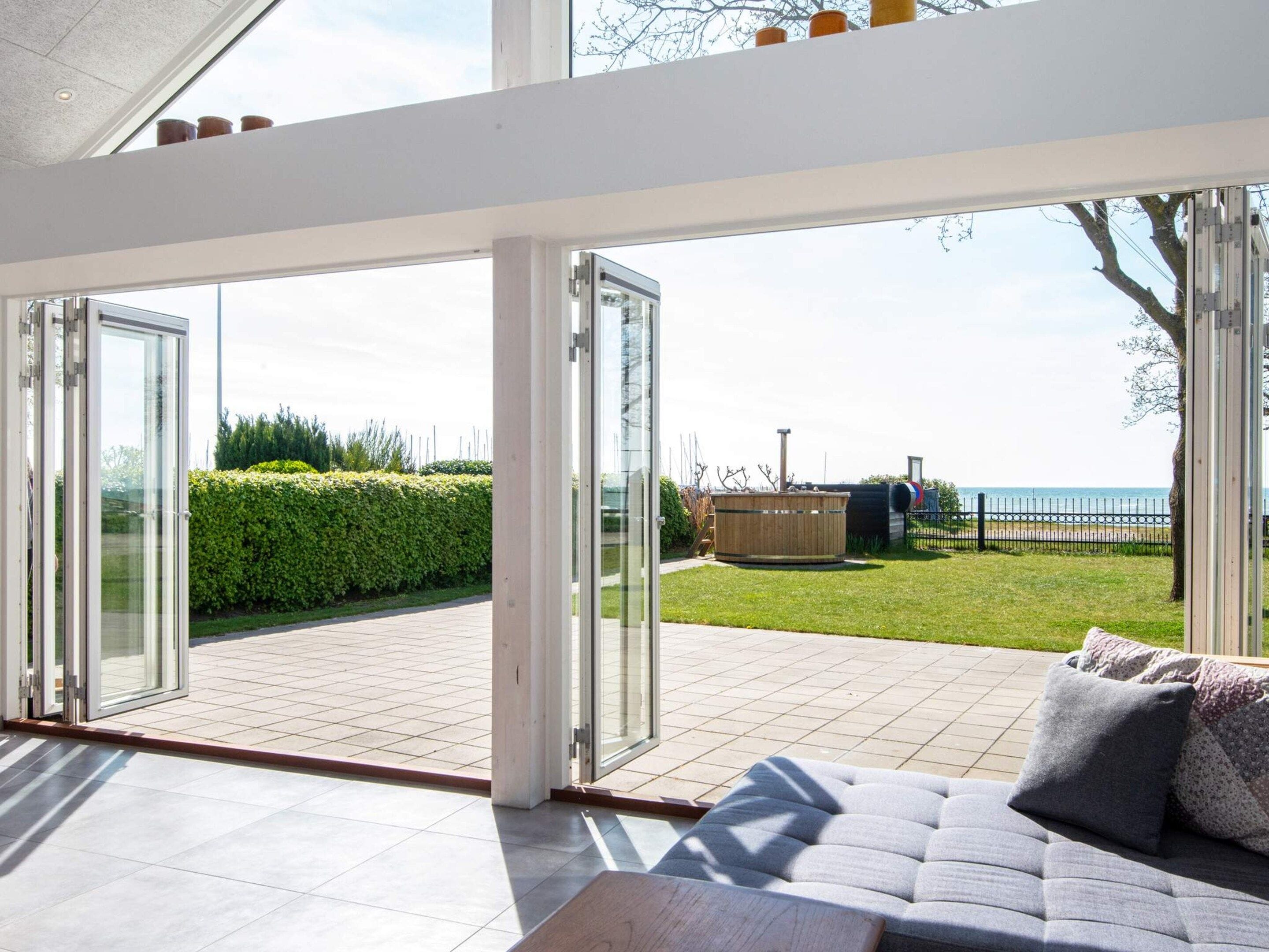 A modern living room with a large glass door leading to a patio area with a view of the sea.