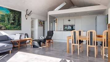 A modern living space with a sofa, a dining table with chairs, a kitchen area, and a large painting on the wall.