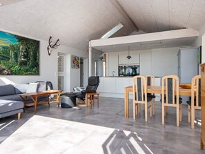 A modern living space with a sofa, a dining table with chairs, a kitchen area, and a large painting on the wall. - 8 Person Holiday Home in Odder (Odder)