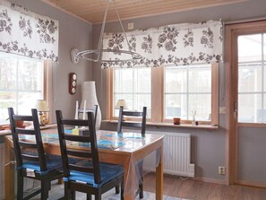 Un comedor con una mesa de madera, sillas y una ventana con cortinas florales.