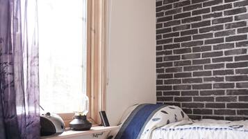 A room with a bed, a window with curtains, a brick wall, and a radiator.