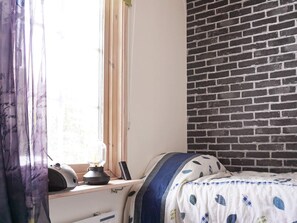 Una habitación con una cama, ventana con cortinas, pared de ladrillo y radiador.