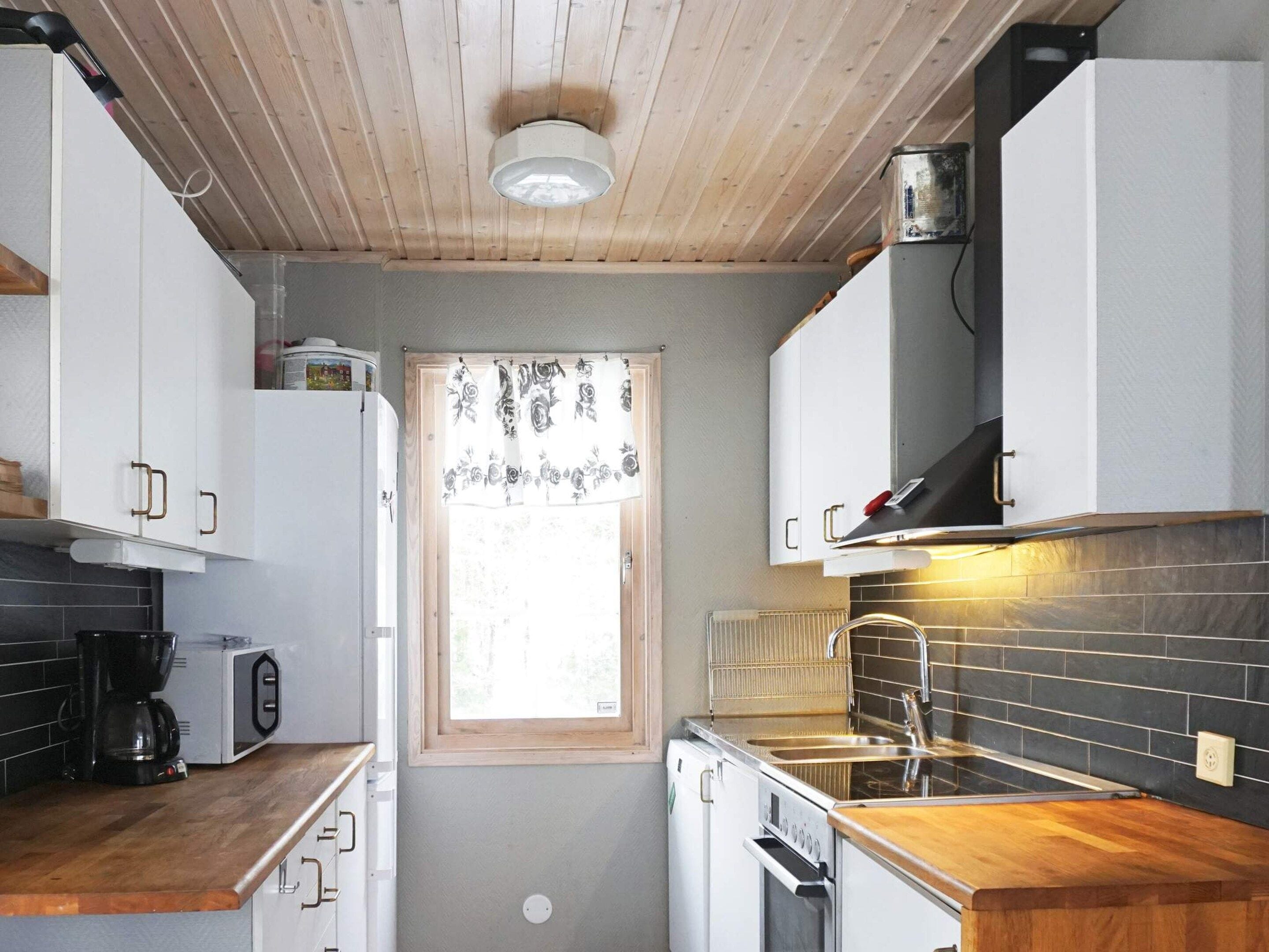A compact kitchen with white cabinets, a wooden countertop, a built-in oven, and a window with a floral curtain.