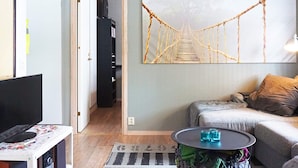 A living room with a sofa, a coffee table, a TV, and a large wall art of a rope bridge. - 3 Person Holiday Home in Munkedal (Munkedal)