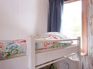 En køjeseng med blomstret sengetøj og et vindue med udsigt til grøn natur.