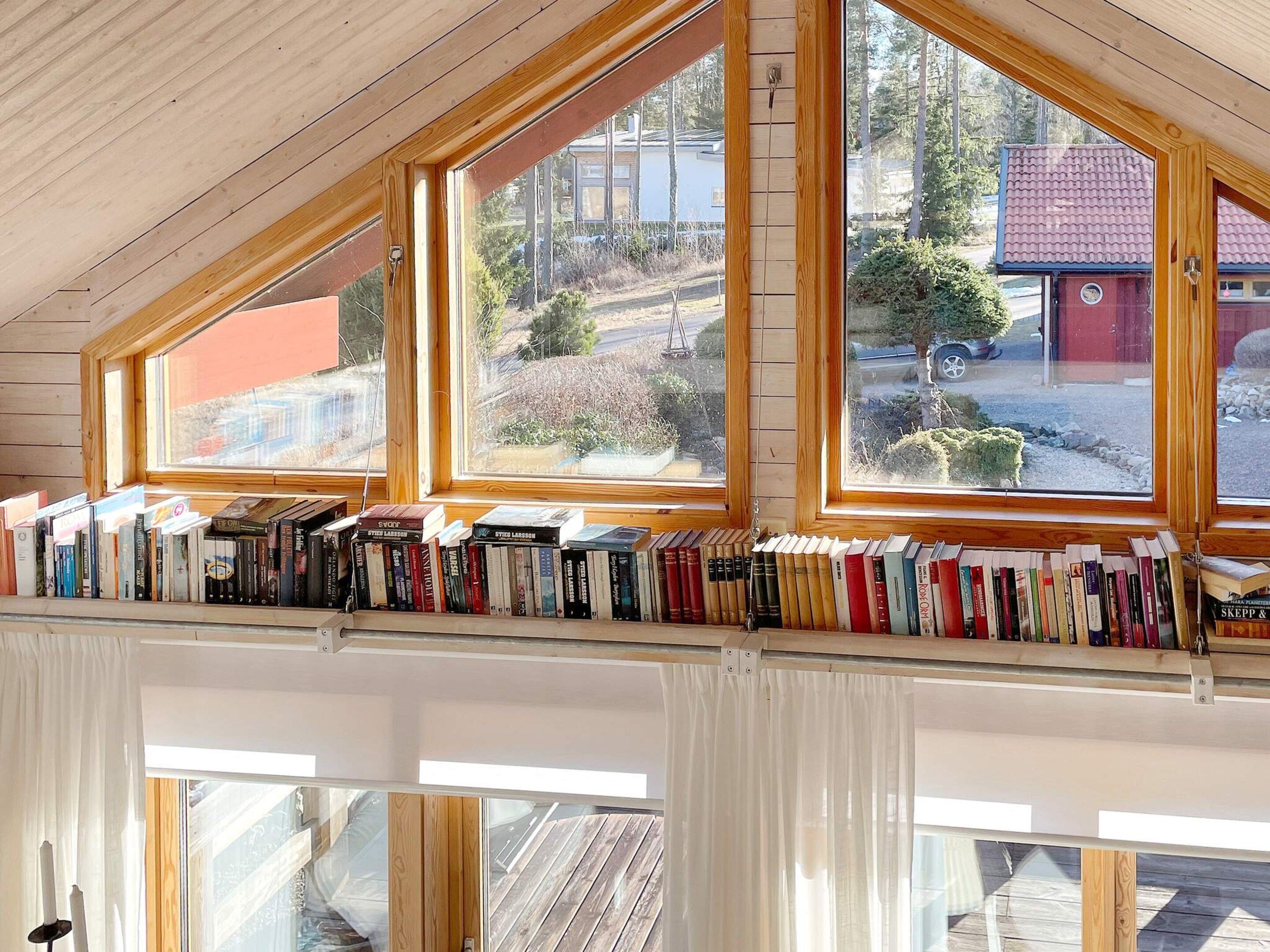 Ein Zimmer mit schrägem Dach, Holzbalken und einem Bücherregal voller Bücher.