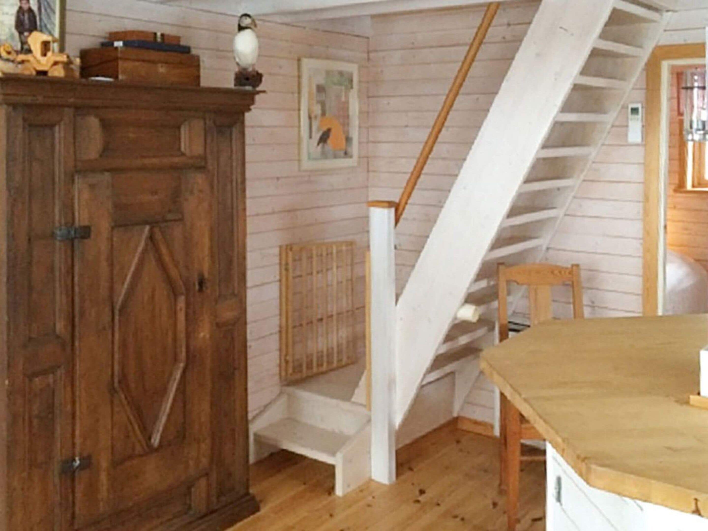 Una habitación con un armario de madera, un cuadro, una escalera y una mesa.