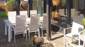 An outdoor patio with white chairs and tables, surrounded by potted plants and a hanging basket. - 5 Star Holiday Home in Forslov (Förslöv)