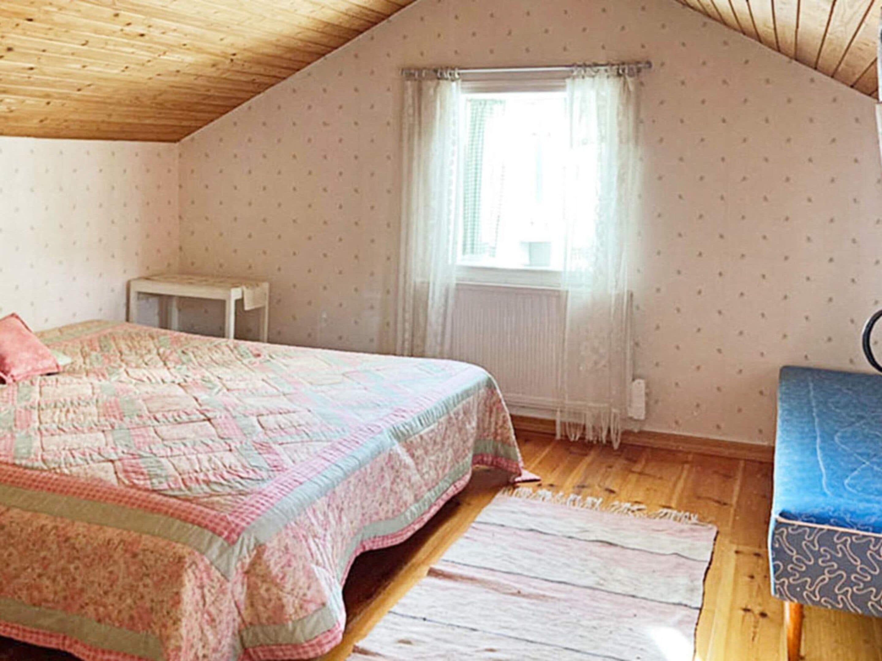 A bedroom with a bed, a small table, a window with curtains, and a radiator.