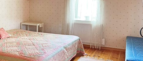 Una camera da letto con un letto, un tavolino, una finestra con tende e un termosifone.
