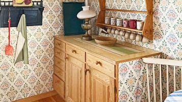 A room with a wooden dresser, a shelf with jars, a hanging towel, and a wall with floral wallpaper.