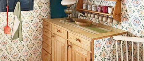 A room with a wooden dresser, a shelf with jars, a hanging towel, and a wall with floral wallpaper.