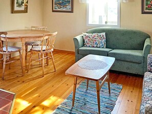 Una sala de estar con una mesa de comedor de madera, sillas, un sofá verde y un tapete estampado.