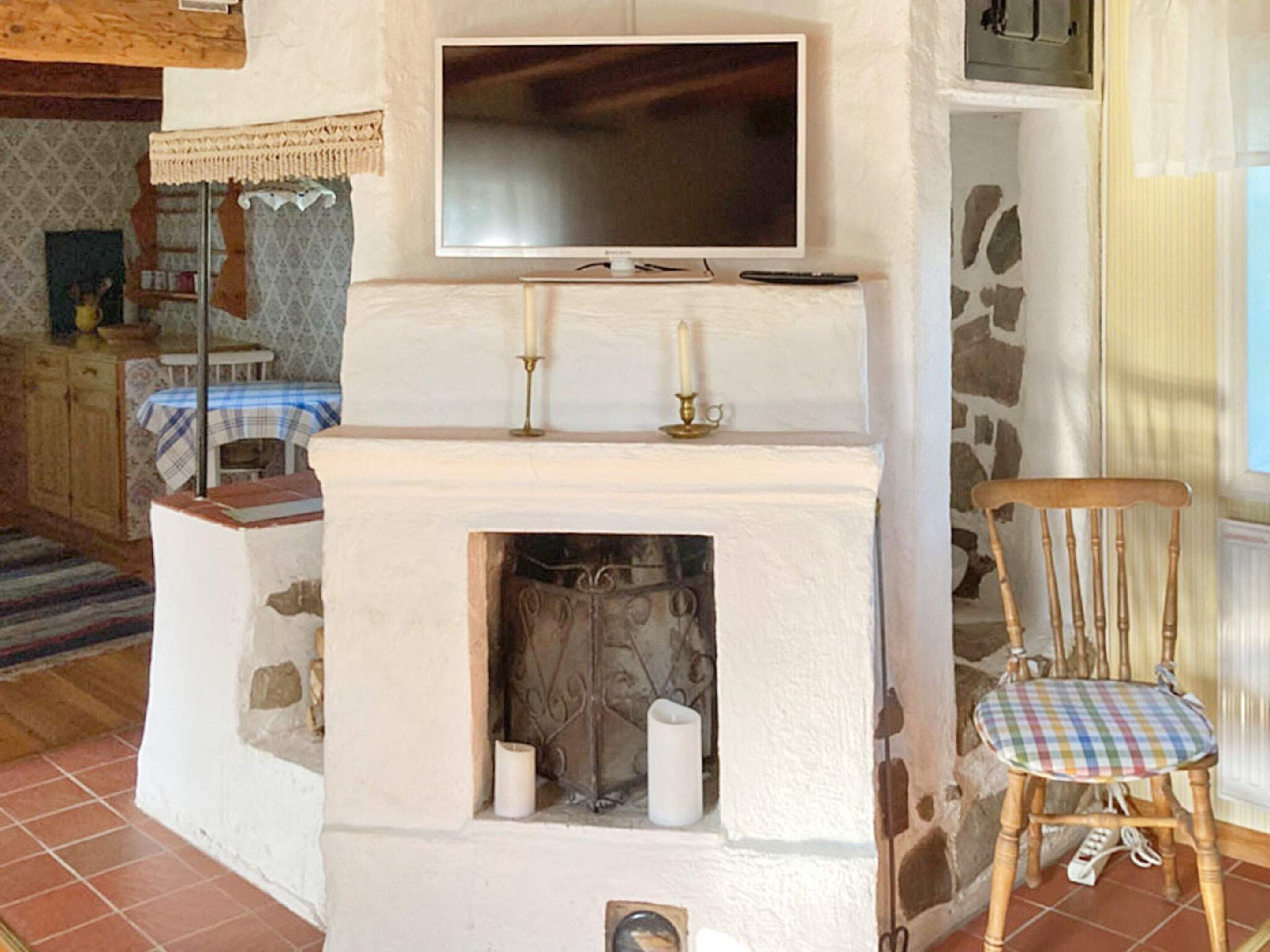 Un salon avec une cheminée, un téléviseur fixé au-dessus, et un fauteuil en bois avec un coussin à carreaux.