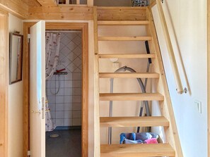 Una escalera de madera que conduce a un piso superior, un baño con cortina de ducha y una tubería de agua visible.