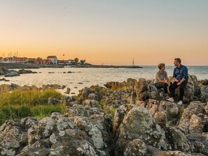 A couple sitting on rocks by a coastal area with a lighthouse in the background. - 4 Person Holiday Home in Svaneke (Svaneke)