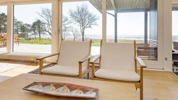 A modern room with two chairs and a table, large windows with a view of the beach, and a covered outdoor area.