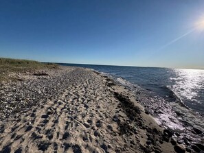En strand med sten og sand, en klar himmel og havet.