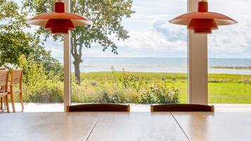 A dining area with a view of the sea, two pendant lights, and a table with chairs.