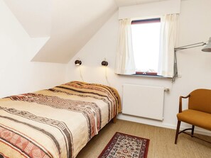 Ein Schlafzimmer mit einem Bett, einem Sessel, einem Fenster mit Vorhängen, einem Heizkörper und zwei Wandlampen.